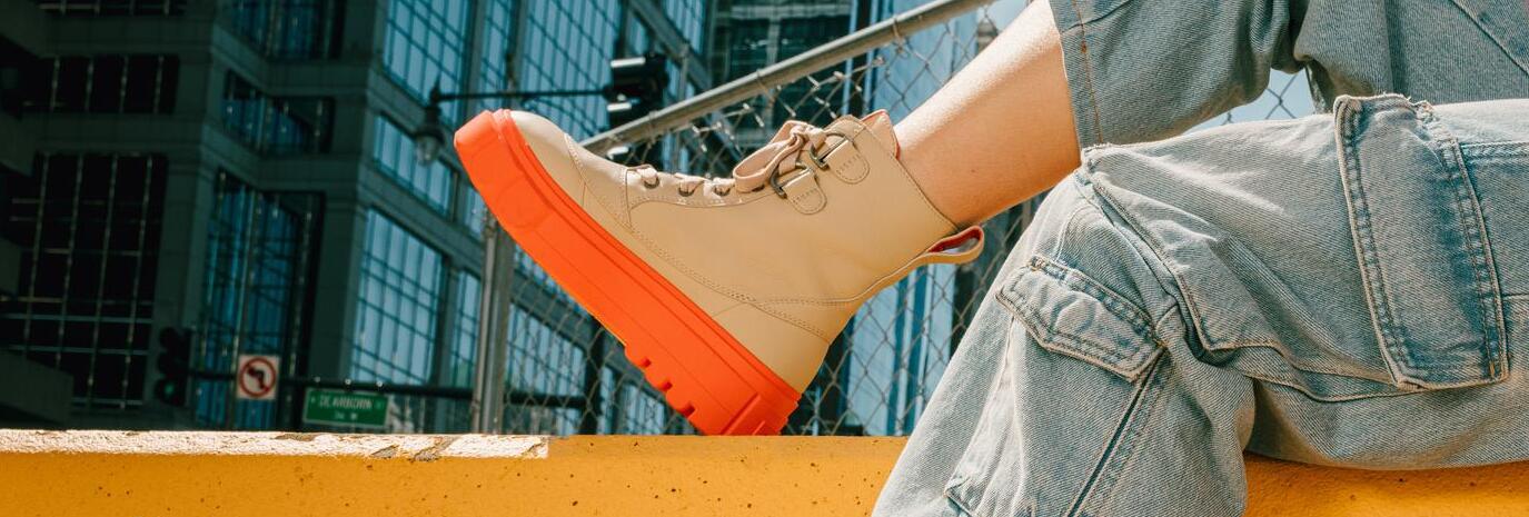 A woman sitting with her foot up on a construction divider wearing Sorel's Caribou X Boot