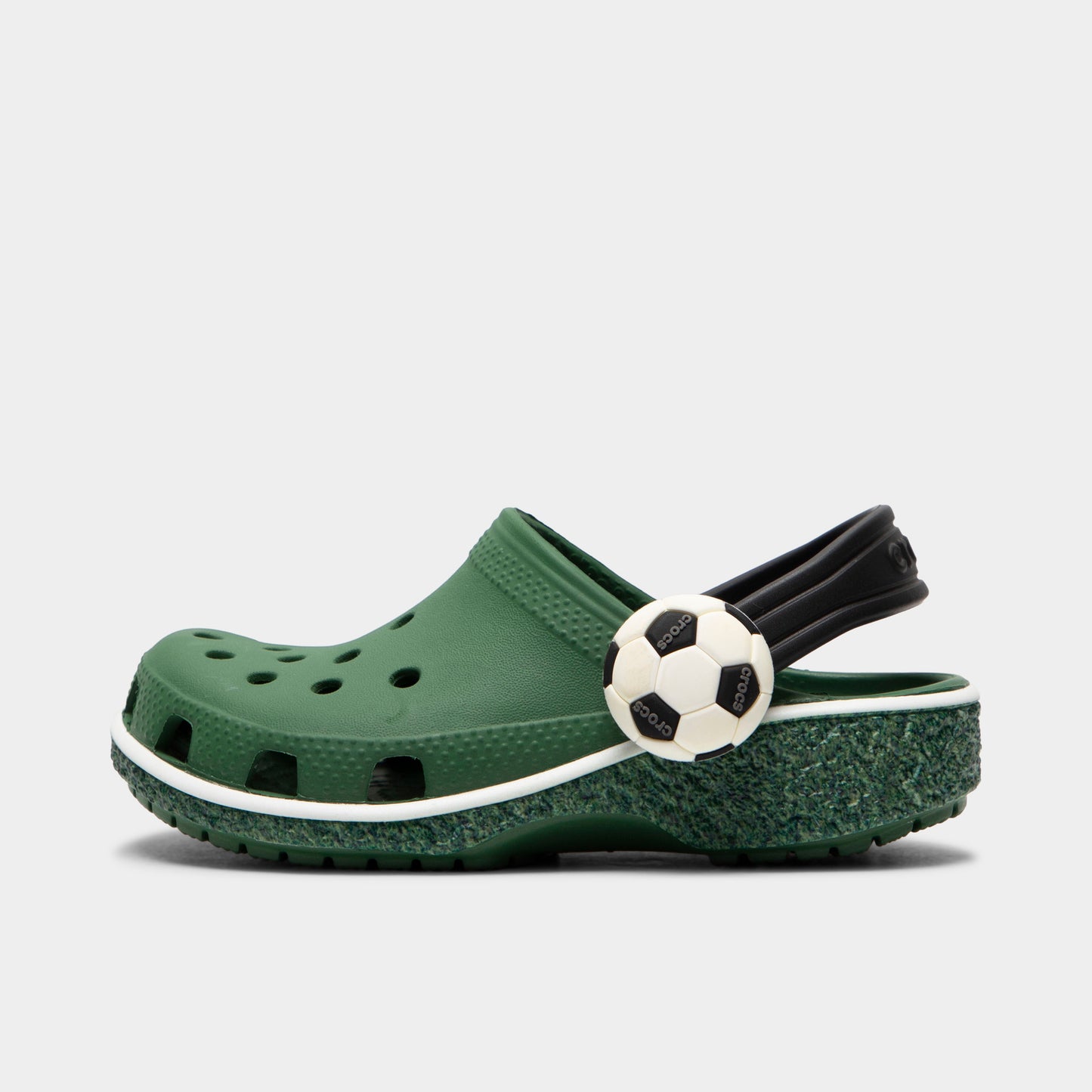Crocs Kids' Classic Funlab Clog. Side view of turf green infant clog with ventilation holes, black heel strap and soccer ball detail.
