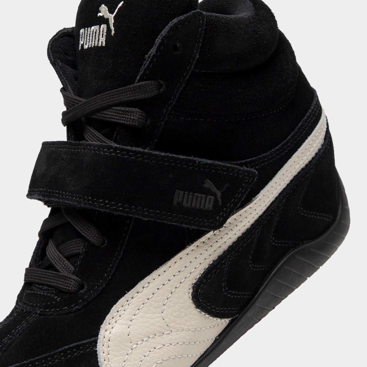 Puma Women's Speedcat Wedge. Close-up of black and white wedge sneaker showing padded tongue, hook-and-loop strap, white Formstrip and stitched panels.
