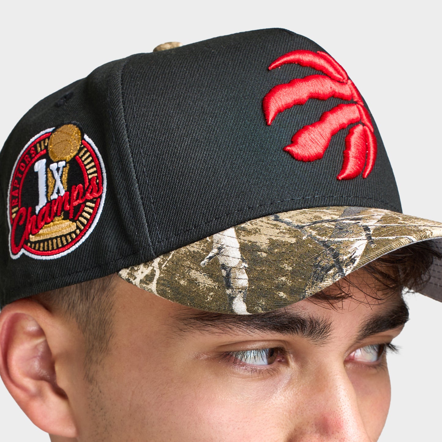 New Era Toronto Raptors 9FORTY AF Snapback. Close-up of black and camo cap showing the red Raptors logo, camouflage brim and embroidered side patch.
