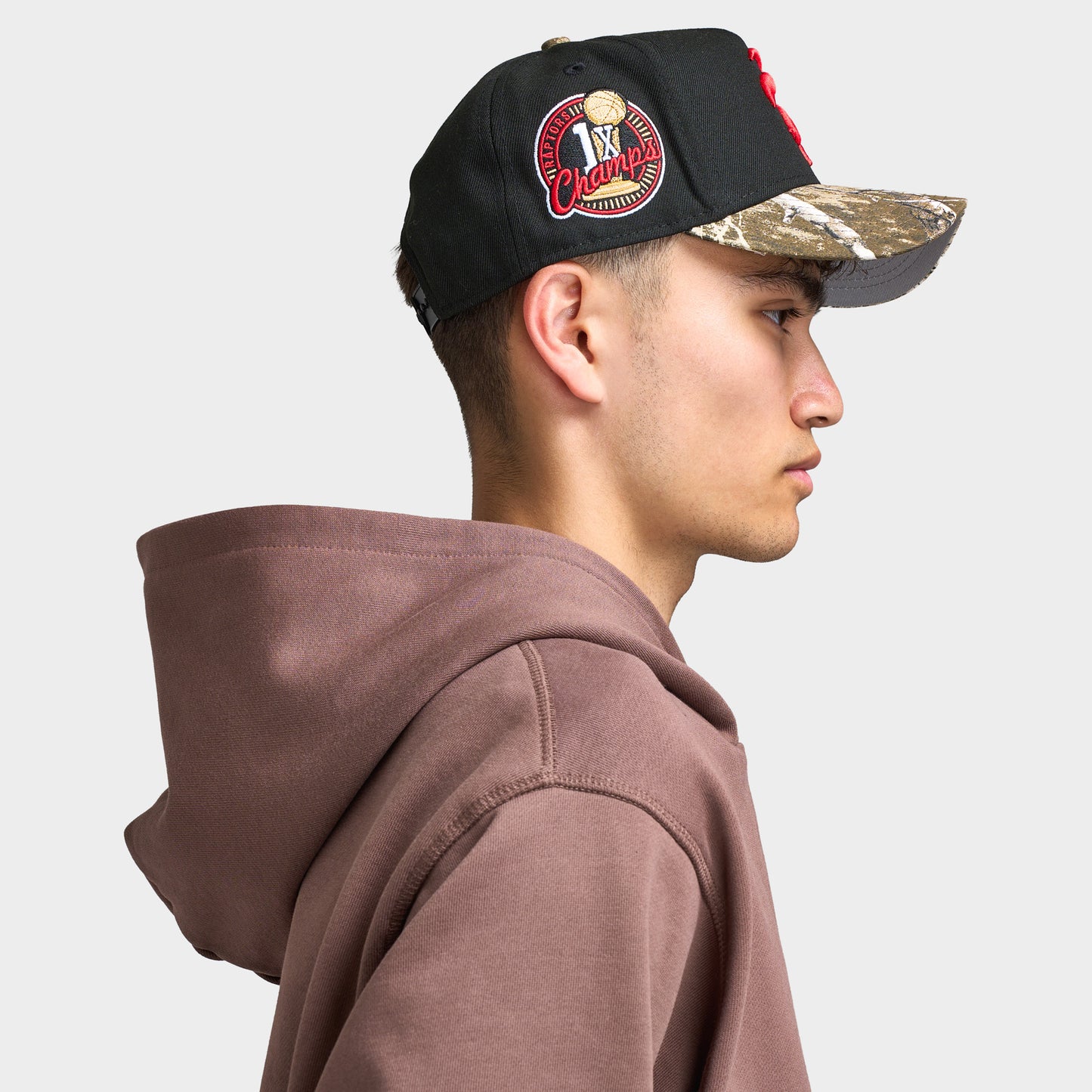 New Era Toronto Raptors 9FORTY AF Snapback. Side view of model wearing black and camo cap with camouflage curved brim, Raptors side patch and structured profile.