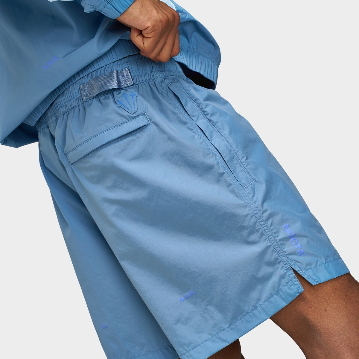 Nike NOCTA Cardinal Nylon Shorts. Close-up view of side hip and thigh highlighting work blue woven nylon fabric, side pocket, back welt pocket tonal NOCTA branding details, and notched hem side vent.