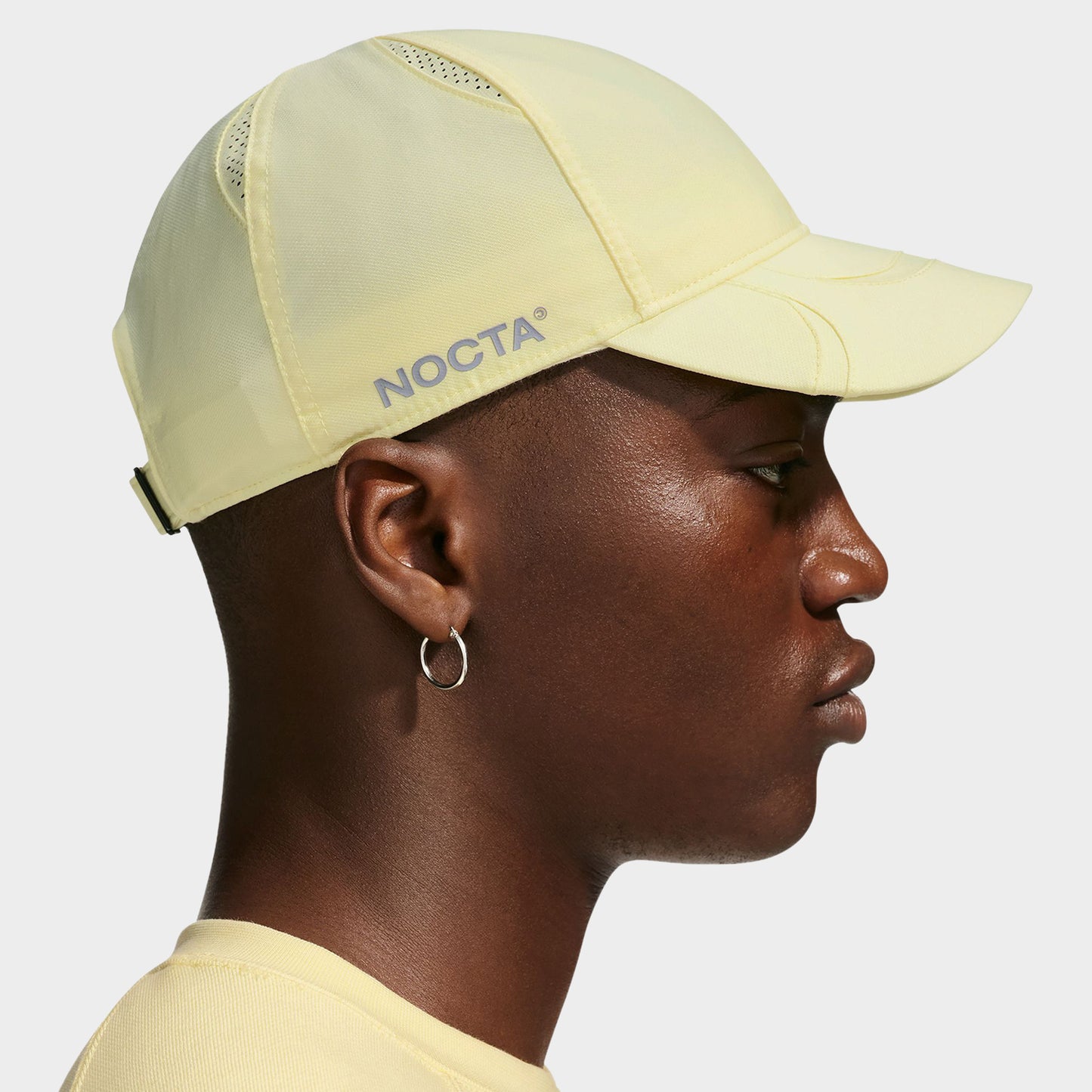 Nike NOCTA S.S.C. Cap CS. Side view of model wearing alabaster and platinum tint cap with curved brim and low-profile crown.
