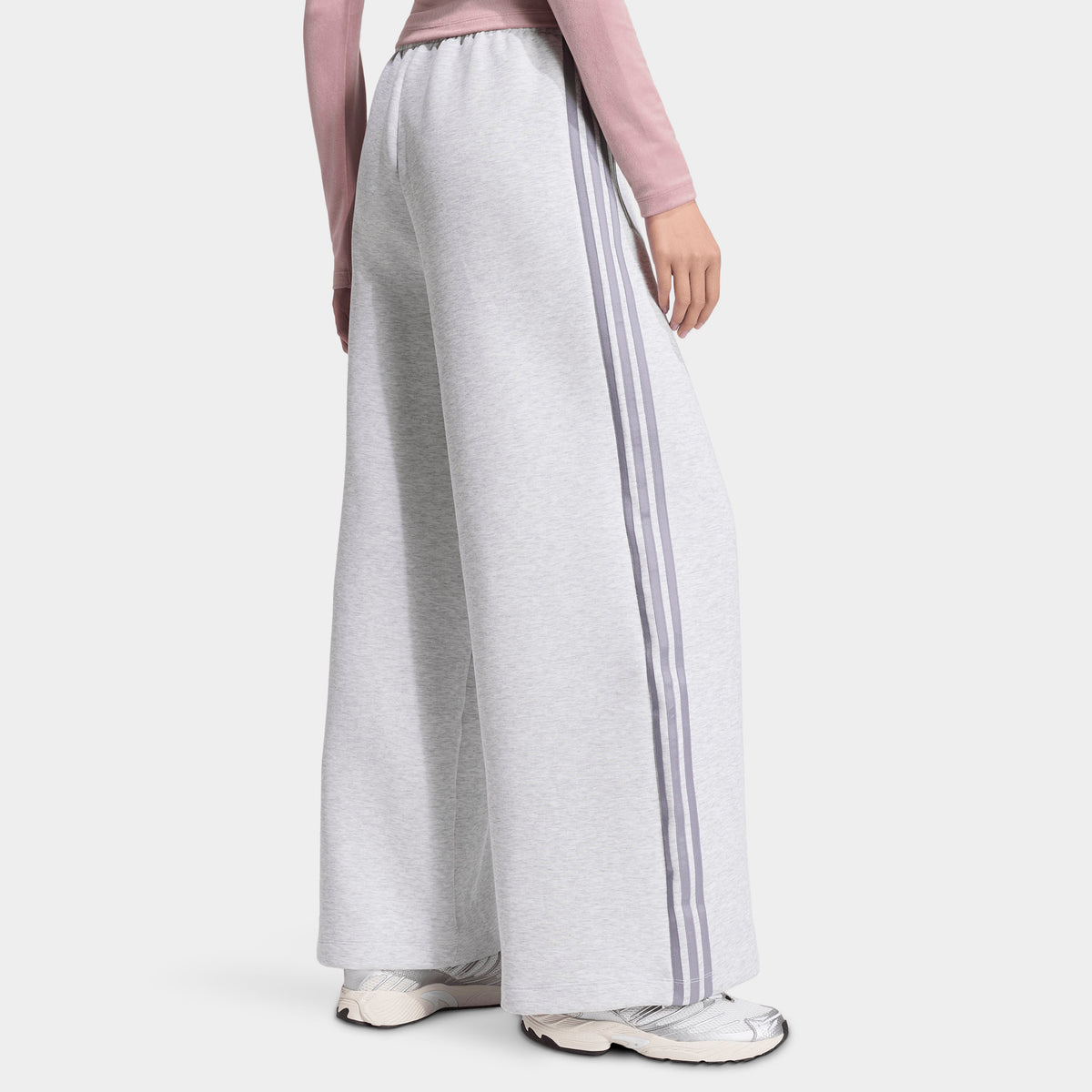 adidas Spacer Track Pants. Side view of model wearing light grey heather and silver track pants with wide legs and white side stripes.