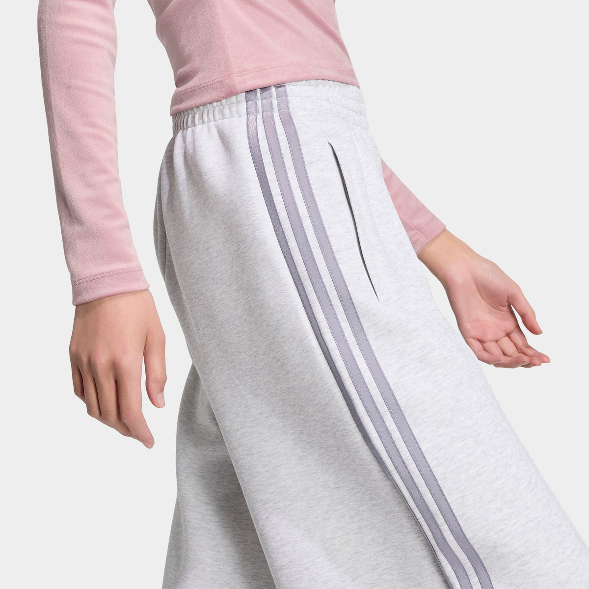 adidas Spacer Track Pants. Three-quarter view of model wearing light grey heather and silver track pants with wide legs and white side stripes.