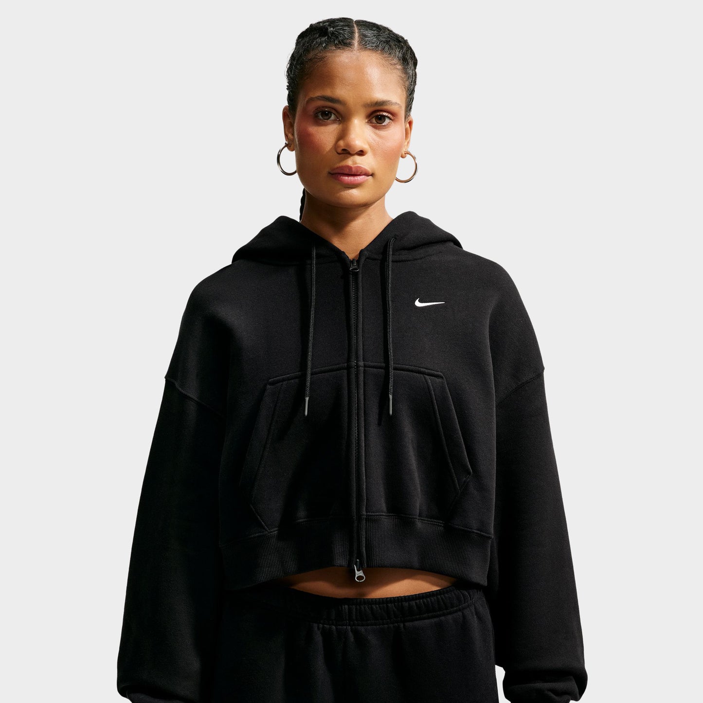 Nike Studio Fleece Cropped Full Zip Hoodie. Front view of model wearing black cropped hoodie with full-zip closure, drawstring hood and small white Nike Swoosh.