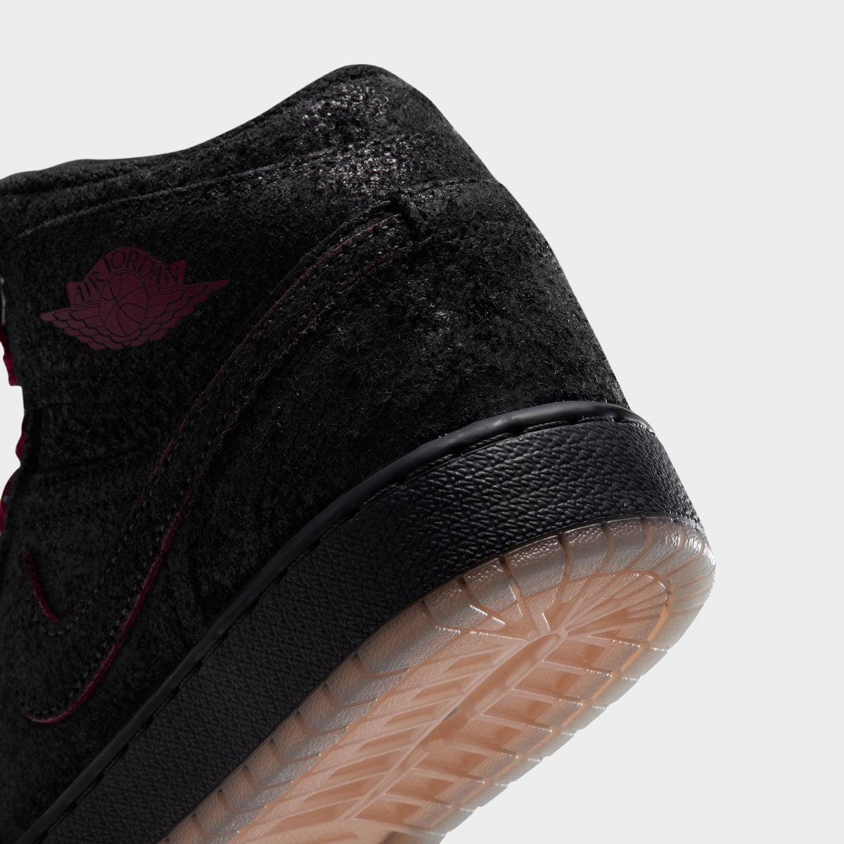 Jordan 1 Mid SE GS. Close-up view showing black textured collar, embossed team red Wings logo, stitched Swoosh, and translucent gum outsole edge.