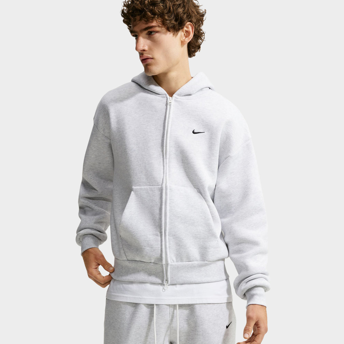 Nike Solo Fleece Full-Zip Hoodie. Birch heather grey fleece hoodie featuring full zip front closure, split kangaroo pocket, ribbed cuffs, and black embroidered chest Swoosh.