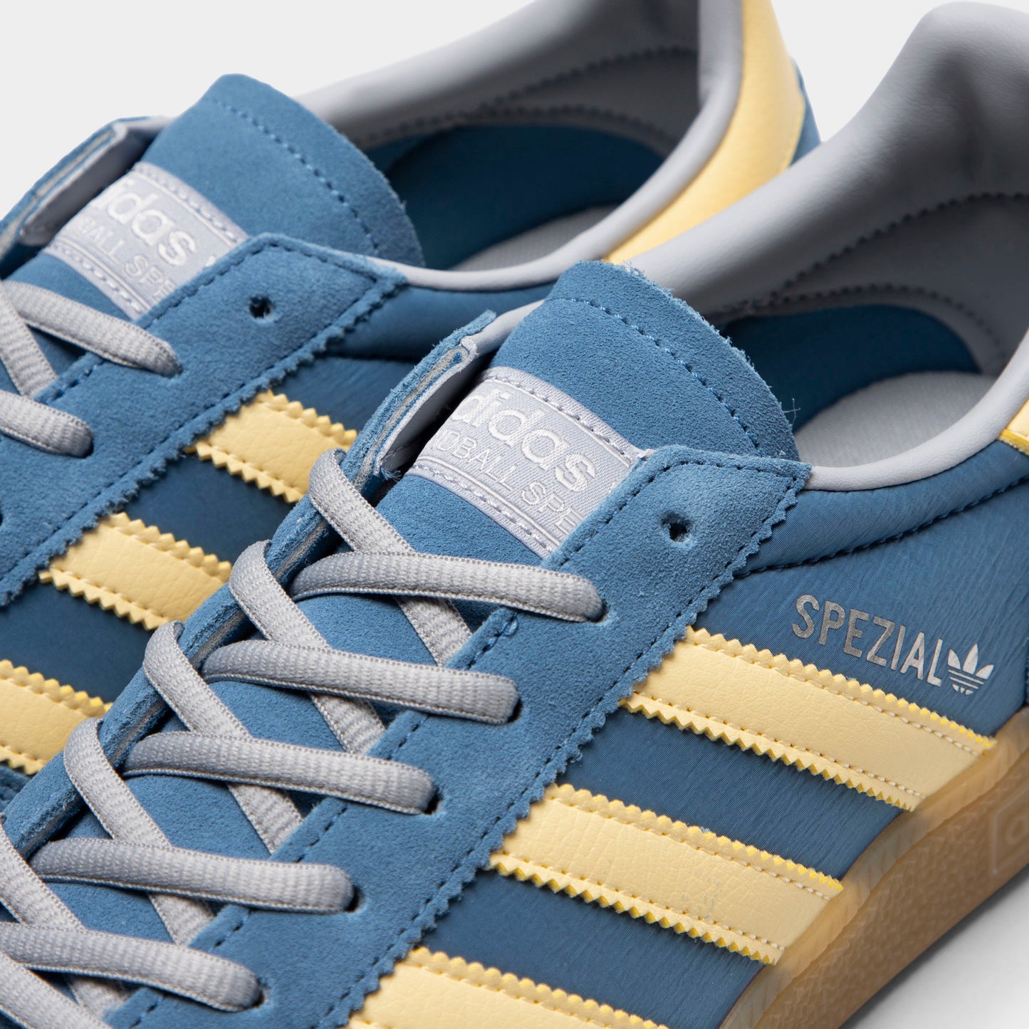 adidas Handball Spezial. Close-up of dusky ink, easy yellow and gum sneaker showing blue laces, yellow three stripes and gold Spezial branding.