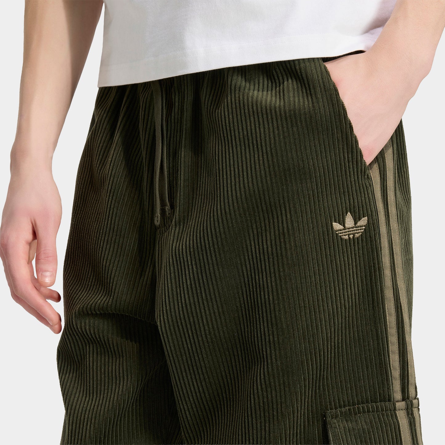 adidas Adicolor Cord Cargo Pants. Close-up of night cargo corduroy pants showing side pocket, Trefoil logo and ribbed texture.