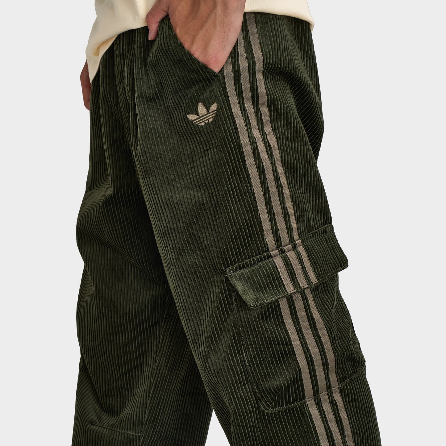 adidas Adicolor Cord Cargo Pants. Close-up of night cargo corduroy pants showing side cargo pocket, tonal three stripes and small Trefoil logo.