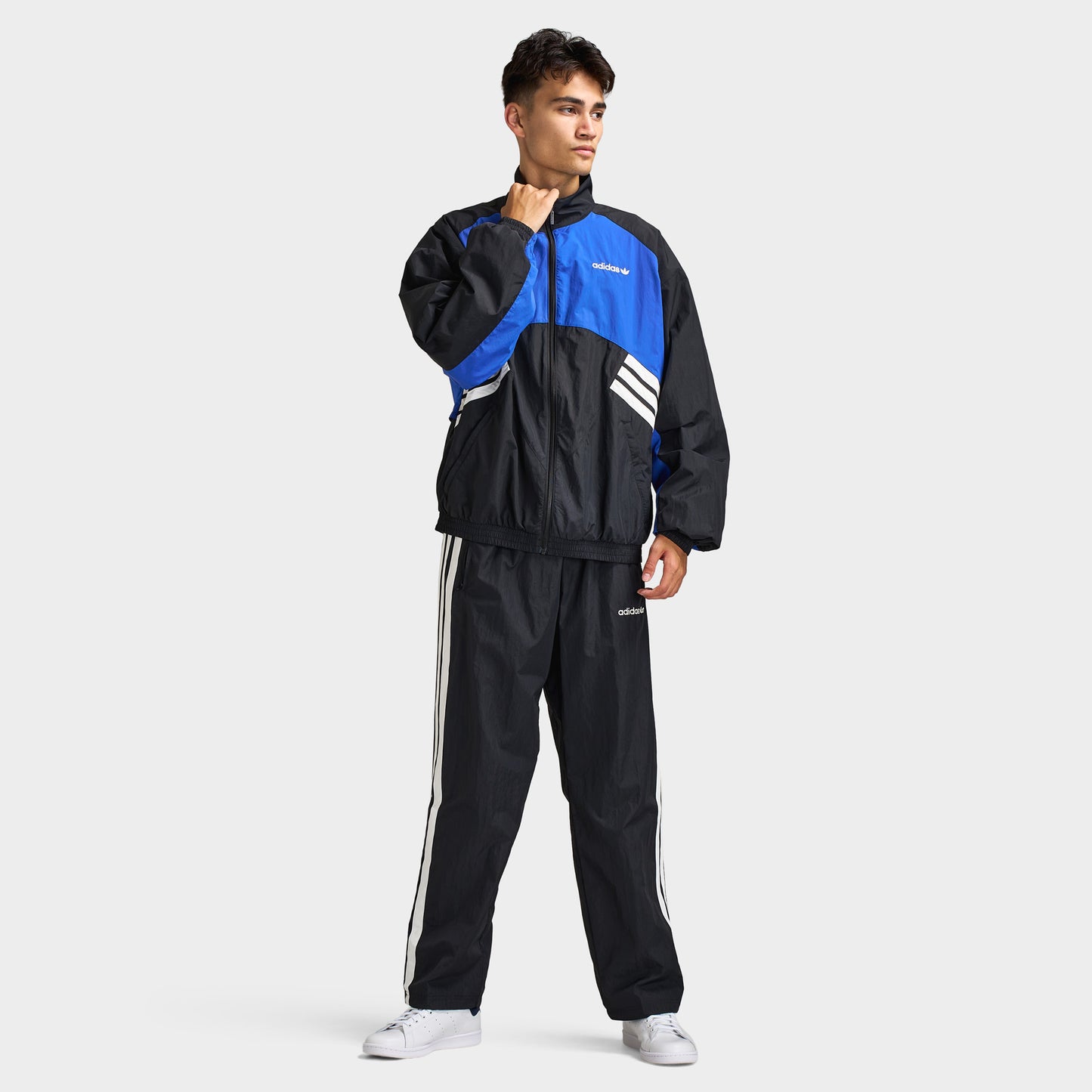 adidas Munich 93 Tracktop. Full-body view of model wearing blue and black track jacket with matching black pants and white sneakers.