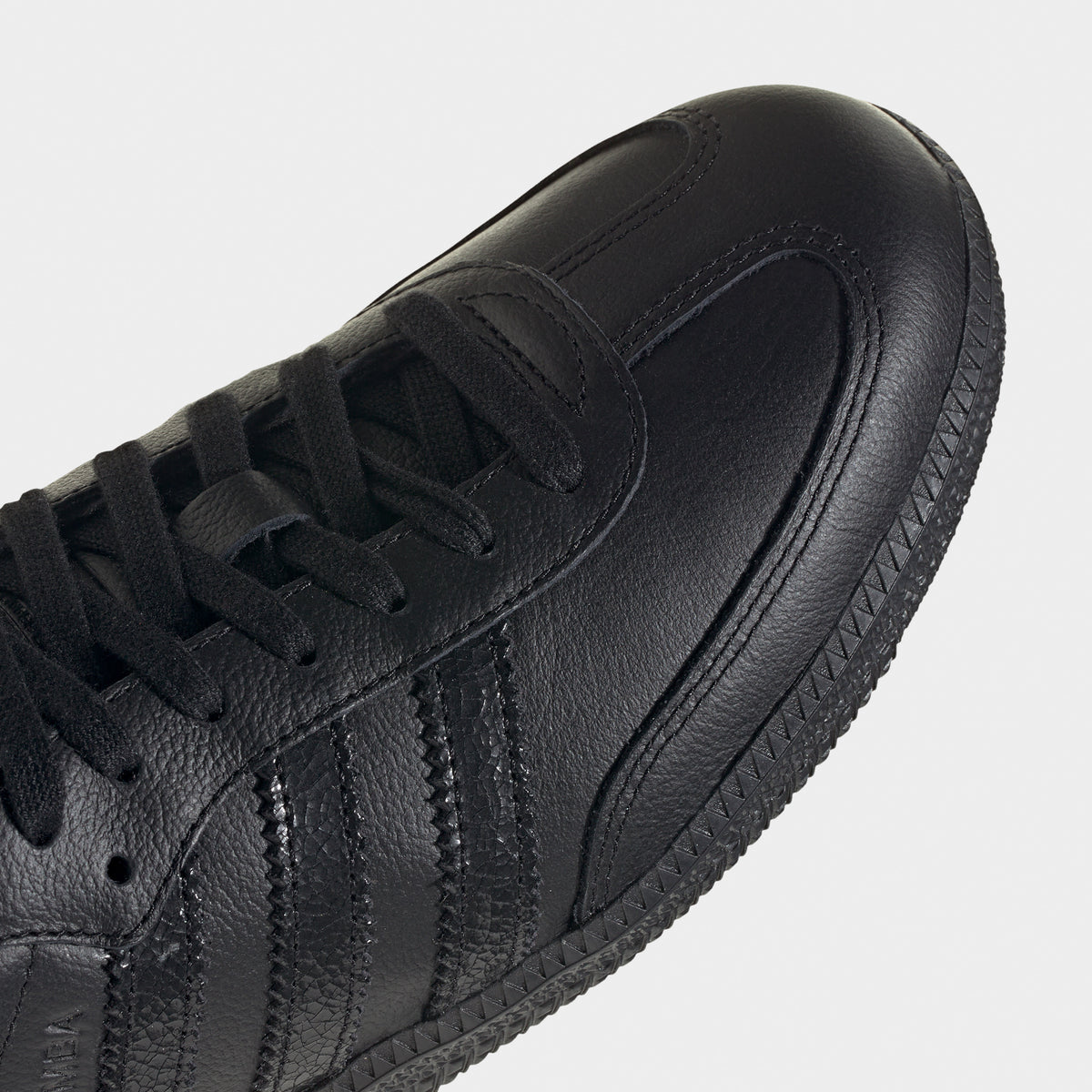 adidas Samba OG. Close-up of black sneaker showing black laces, tonal three stripes, stitched toe panel and textured upper.