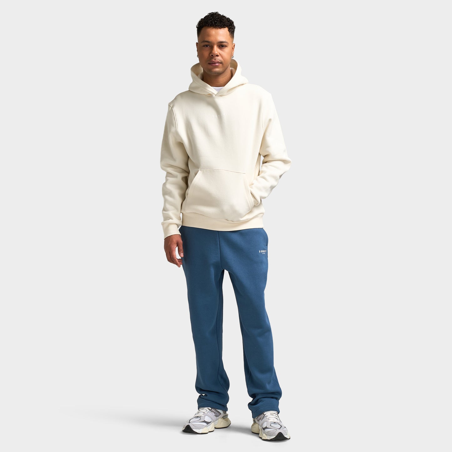 Sonneti London Hoodie 2.0. Full-body front view of model wearing egret hoodie with blue pants and white sneakers.