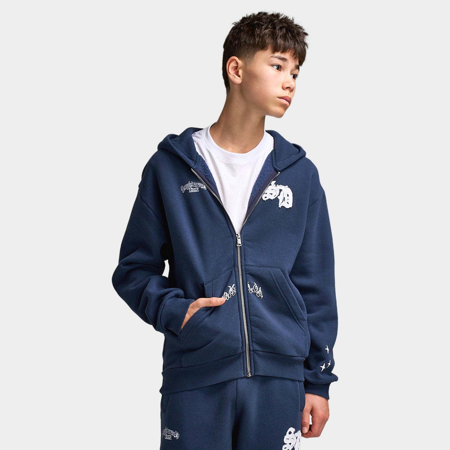 Supply & Demand Juniors' Scape Hoodie. Front view of model wearing washed navy full-zip hoodie with front pockets and white chest graphic.