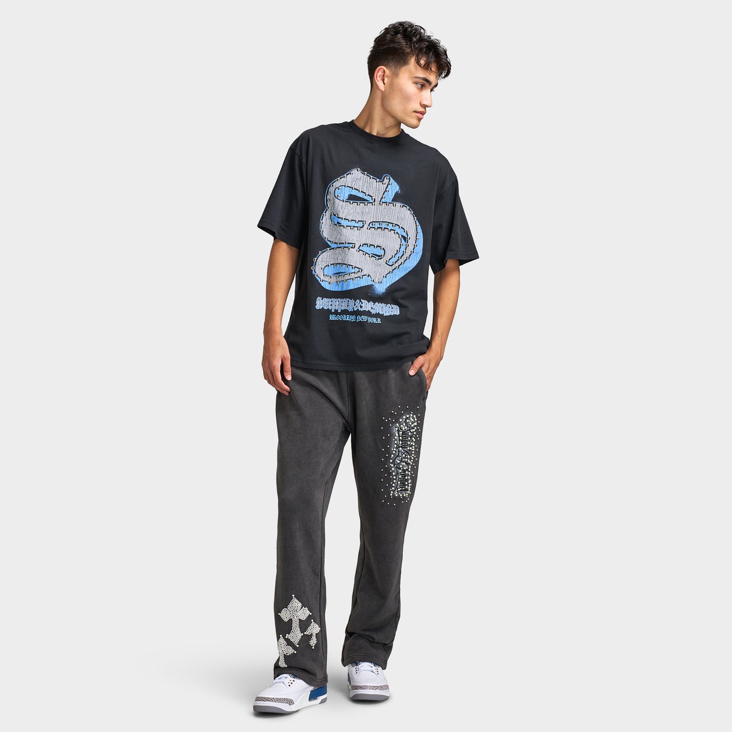 Supply & Demand Murphy Oversized Pants. Full-body view of model wearing black oversized pants with a graphic T-shirt and sneakers.