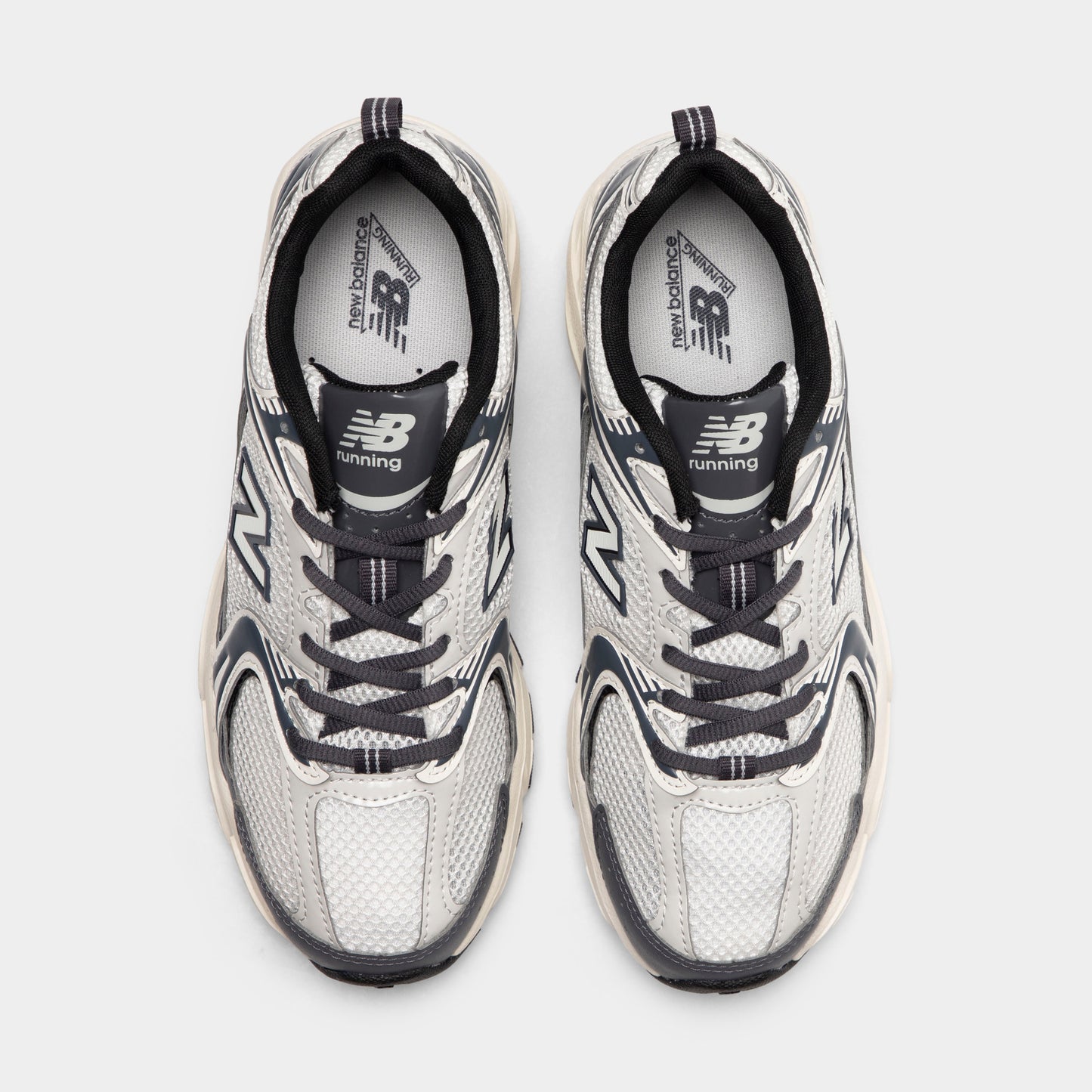 New Balance 530. Top view of sea salt and magnet sneakers showing grey laces, padded tongues and mesh toe boxes.