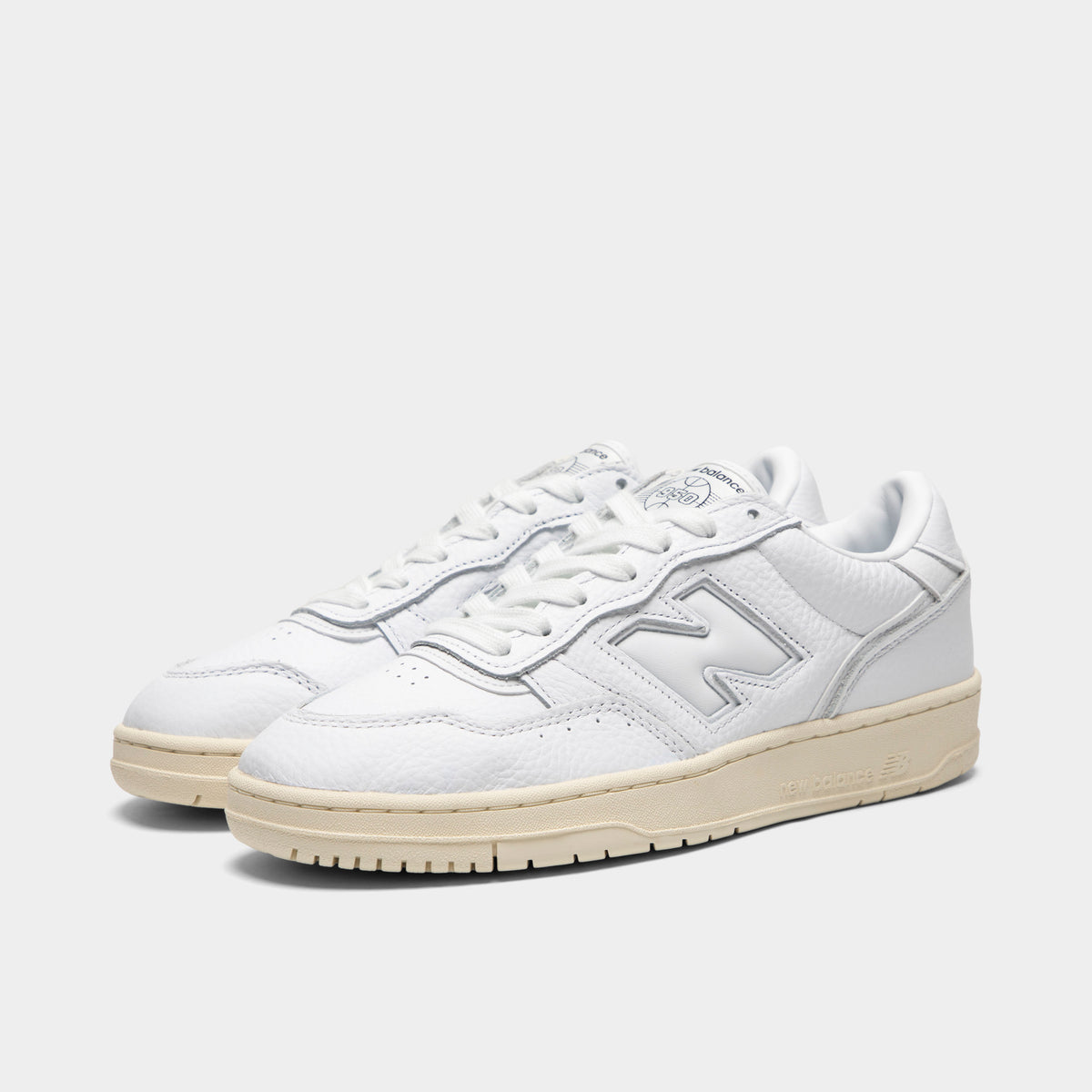 New Balance 950. Three-quarter view of a pair of low-top sneakers showing white leather uppers, midfoot "N" logos, white laces, padded collars, and off-white aged rubber soles.