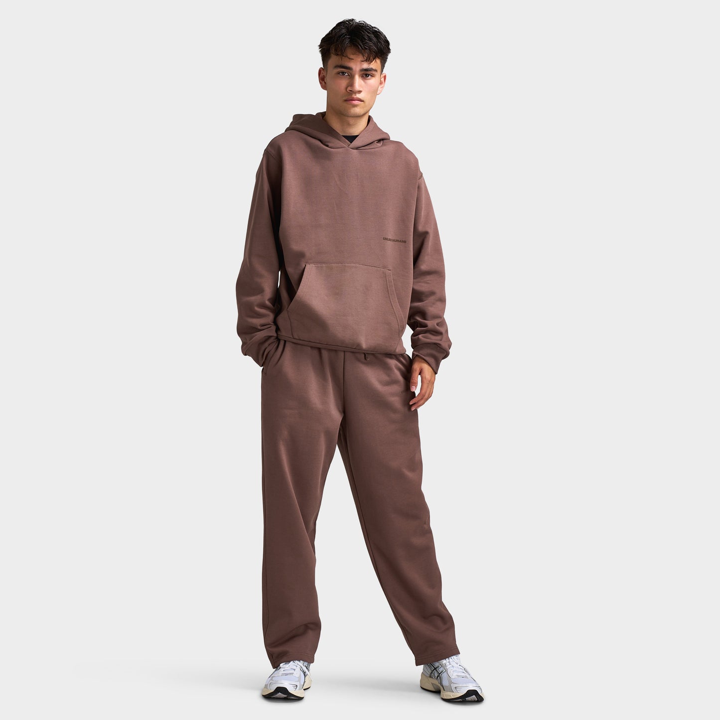 Unlike Humans Ridge Hoodie. Full-body front view of model wearing coffee quarts hoodie with matching pants and dark shoes.