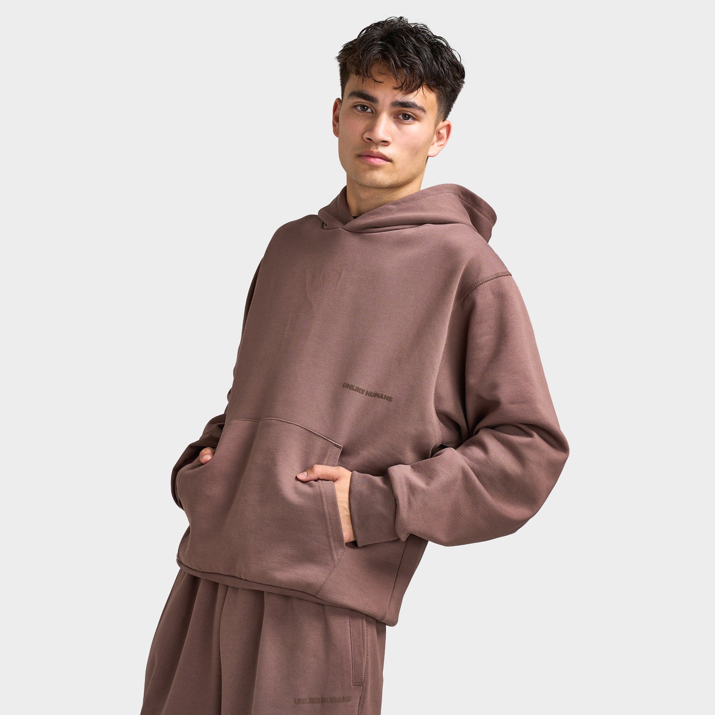 Unlike Humans Ridge Hoodie. Three-quarter view of model wearing coffee quarts hoodie with kangaroo pocket and relaxed sleeves.