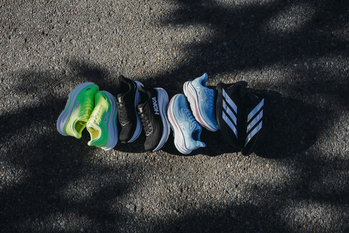 Flat-lay lifestyle photography showcasing a curated lineup of high-performance running shoes arranged horizontally across textured asphalt, captured in dramatic, high-contrast afternoon sunlight with geometric tree shadow overlays.