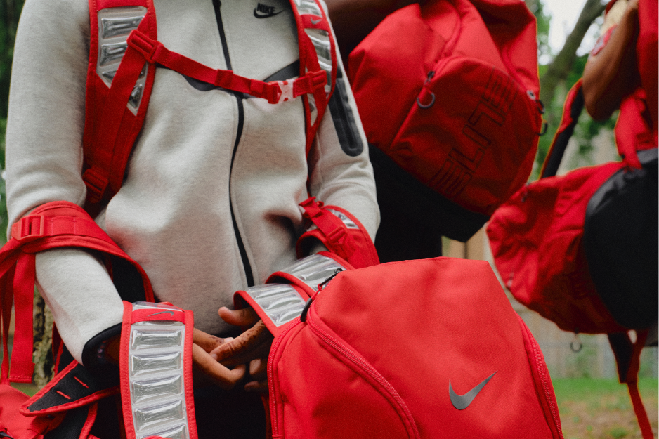 Close-up of person wearing Nike fleece jacket surrounded by red backpacks.