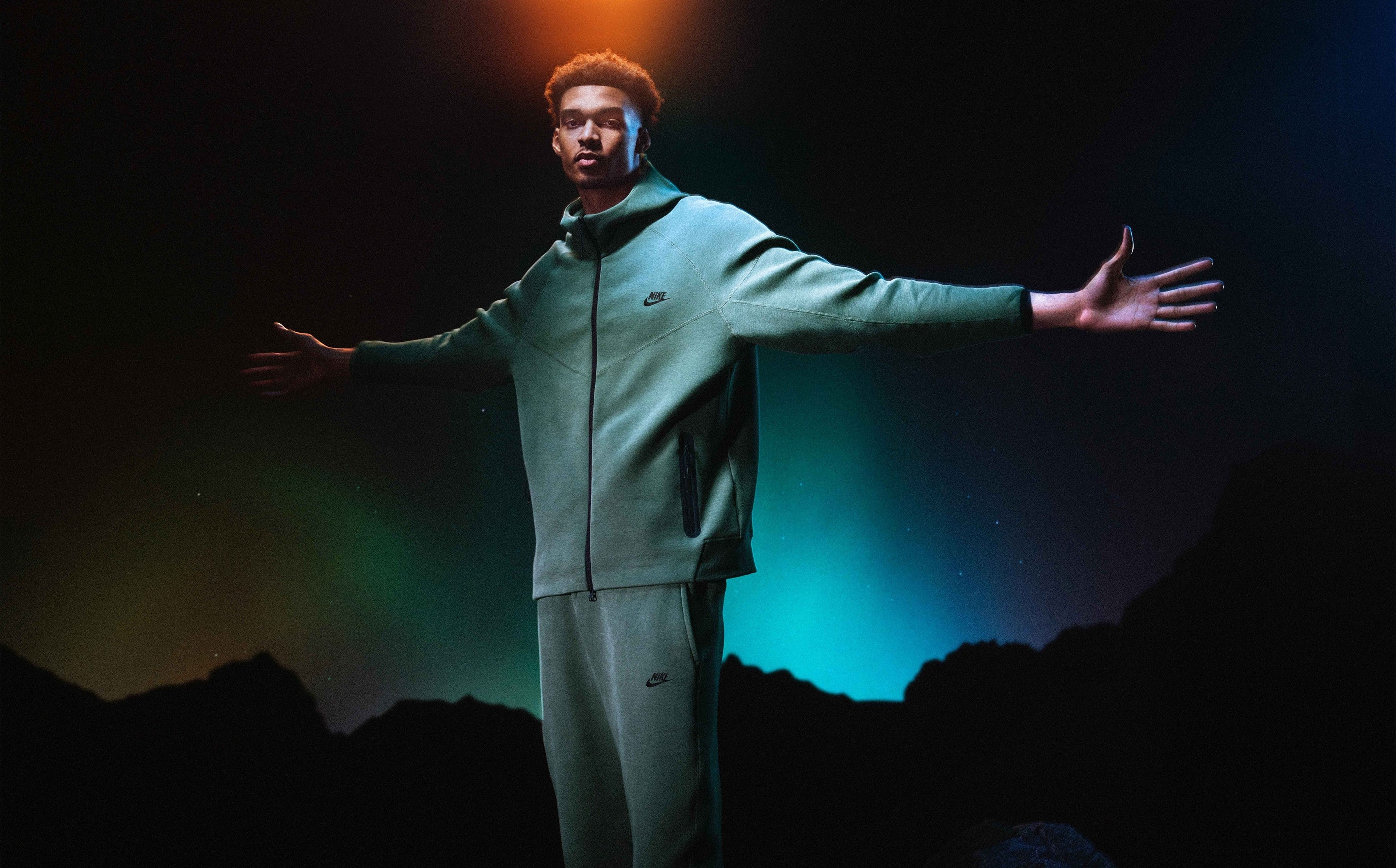 San Antonio Spurs player Victor Wembanyama  opens his arms wide and shows off his matching green Nike Tech Fleece set