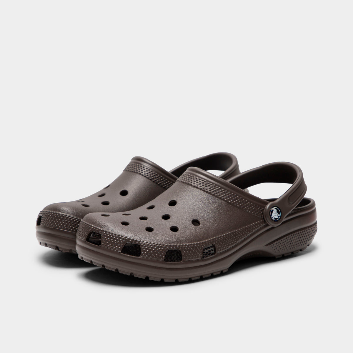 Crocs Classic Clog. Three-quarter view of espresso clogs with ventilation holes, raised heel straps and rounded toes.