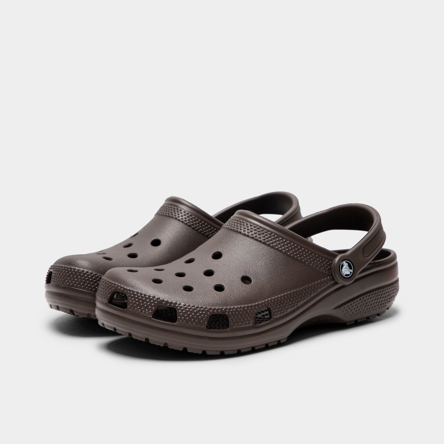 Crocs Classic Clog. Three-quarter view of espresso clogs with ventilation holes, raised heel straps and rounded toes.