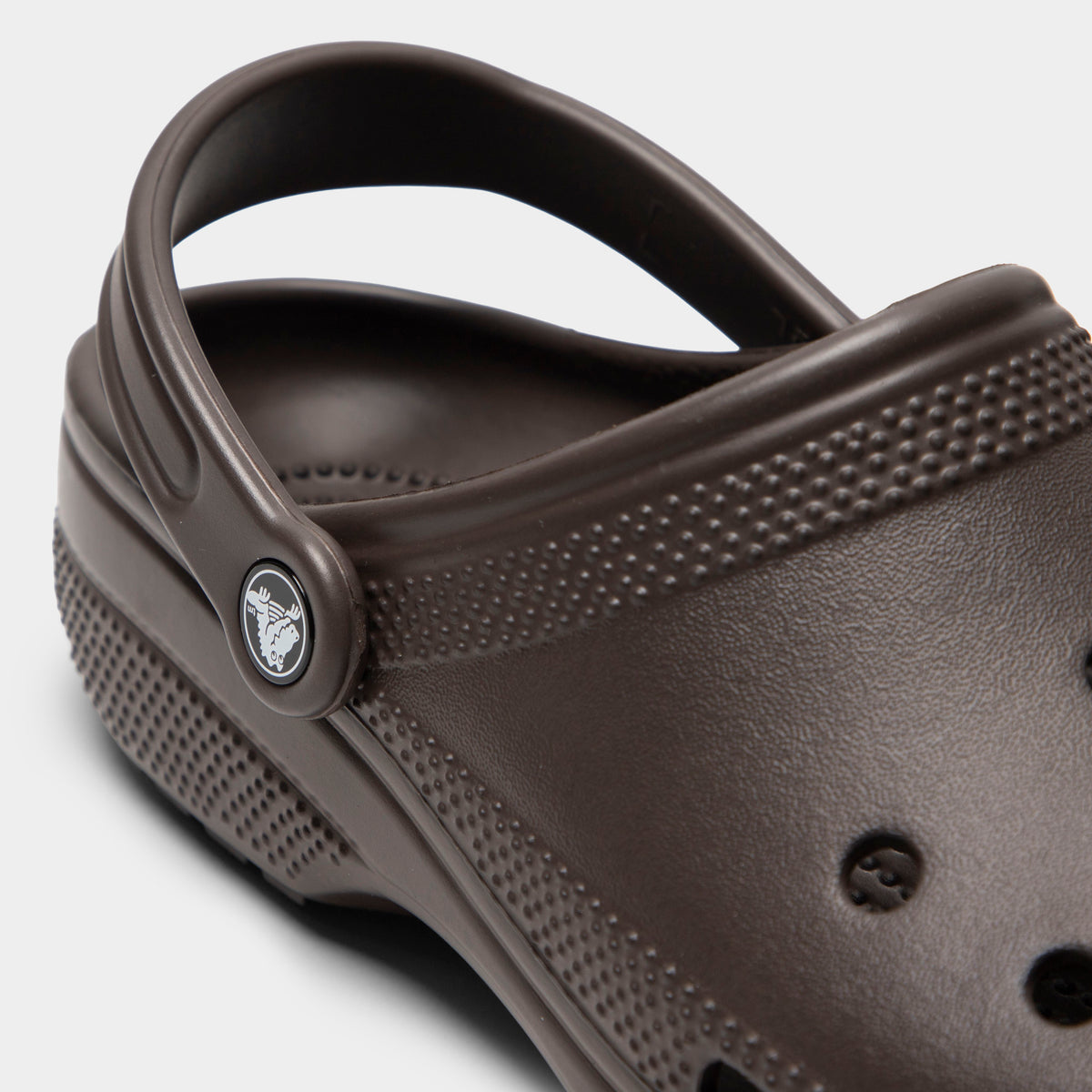 Crocs Classic Clog. Close-up of espresso clog showing pivoting heel strap, Crocs logo button and sculpted side panel.