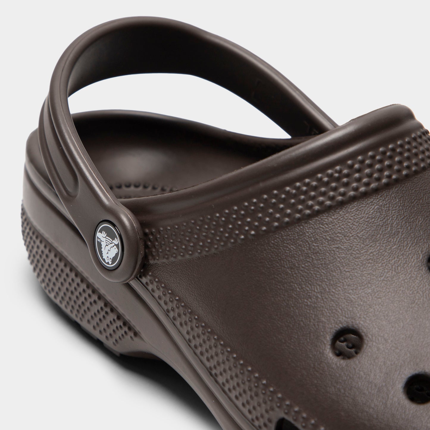 Crocs Classic Clog. Close-up of espresso clog showing pivoting heel strap, Crocs logo button and sculpted side panel.