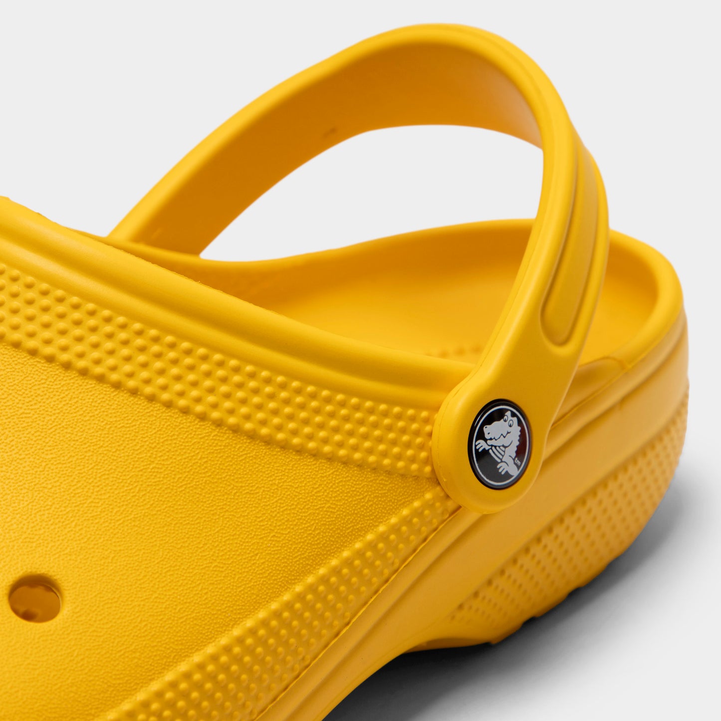 Crocs Classic Clog. Close-up of golden light clog showing pivoting heel strap, Crocs logo button and sculpted side panel.