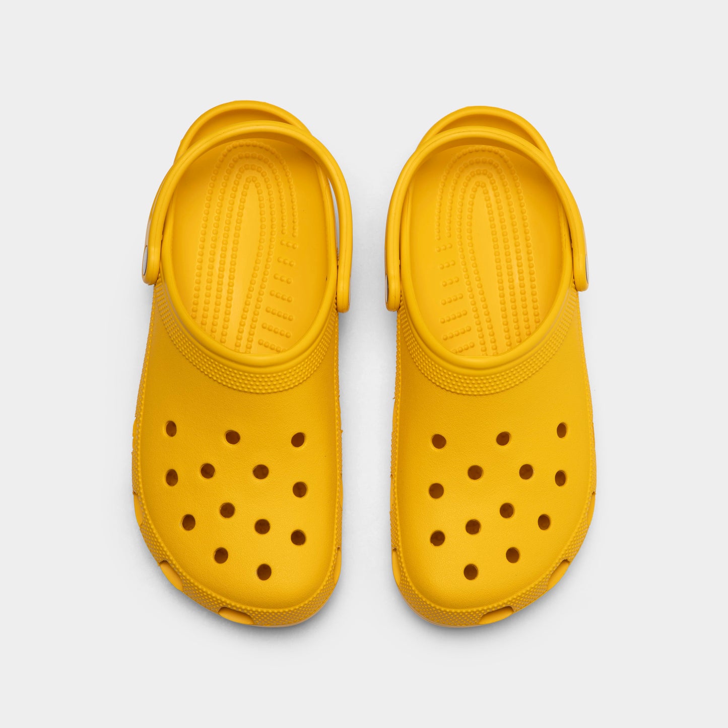 Crocs Classic Clog. Top view of golden light clogs showing ventilation holes, rounded toe boxes and pivoting heel straps.