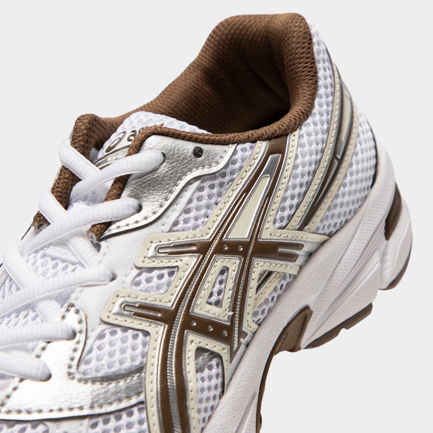 ASICS GEL-1130 GS. Close-up of white and clay canyon sneaker showing white laces, mesh panels, brown ASICS stripes and padded collar.