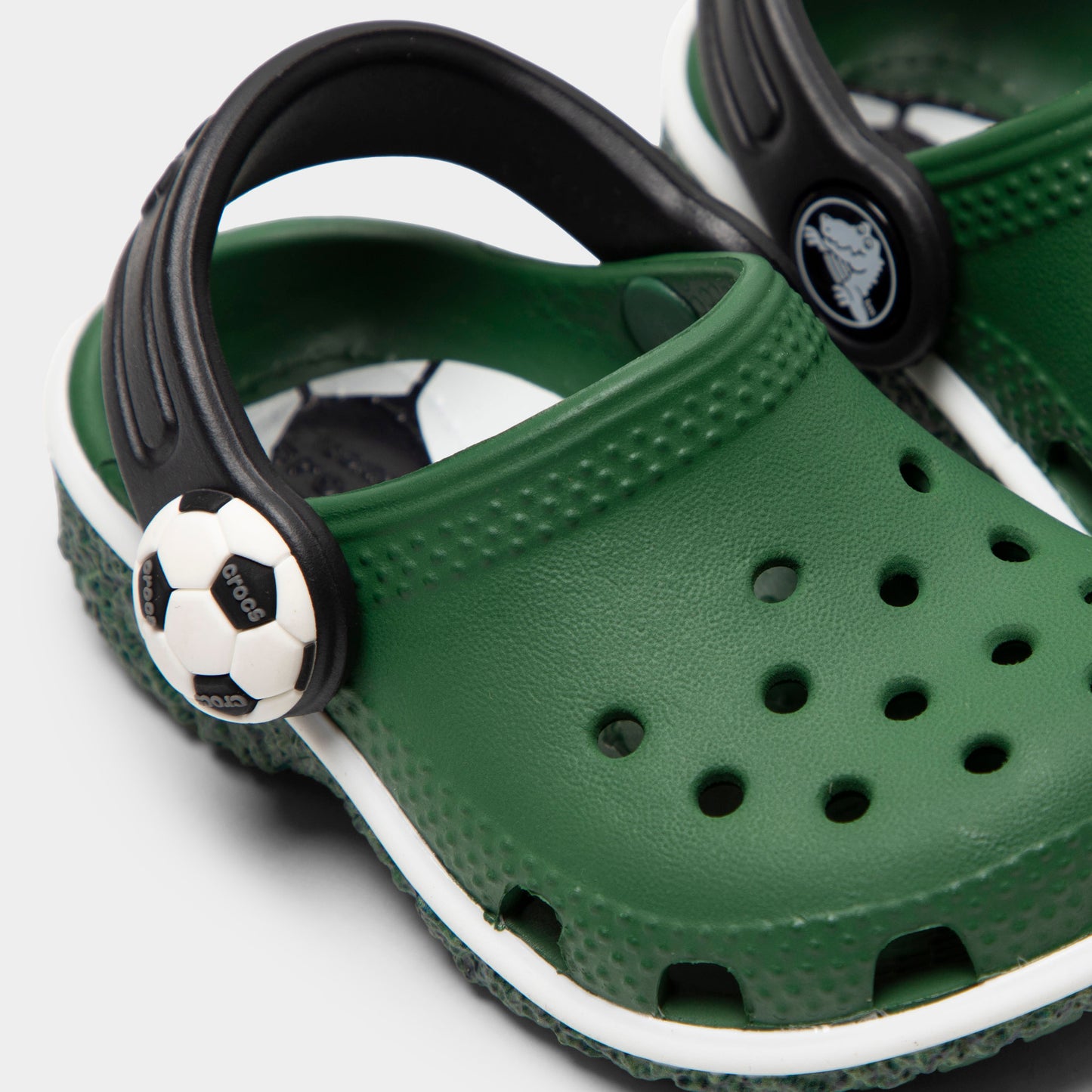 Crocs Infants' Classic Funlab Clog. Close-up of turf green infant clog showing black pivoting heel strap, soccer ball detail and ventilation holes.