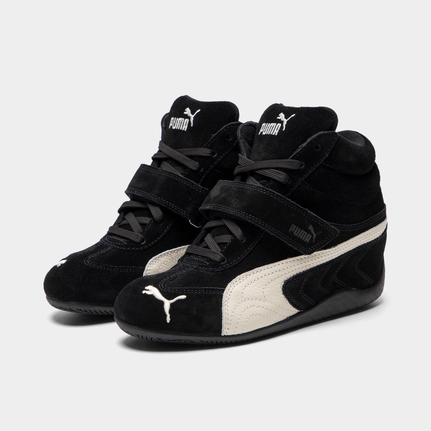 Puma Women's Speedcat Wedge. Three-quarter view of black and white wedge sneakers with padded collars, hook-and-loop straps and white Formstrips.