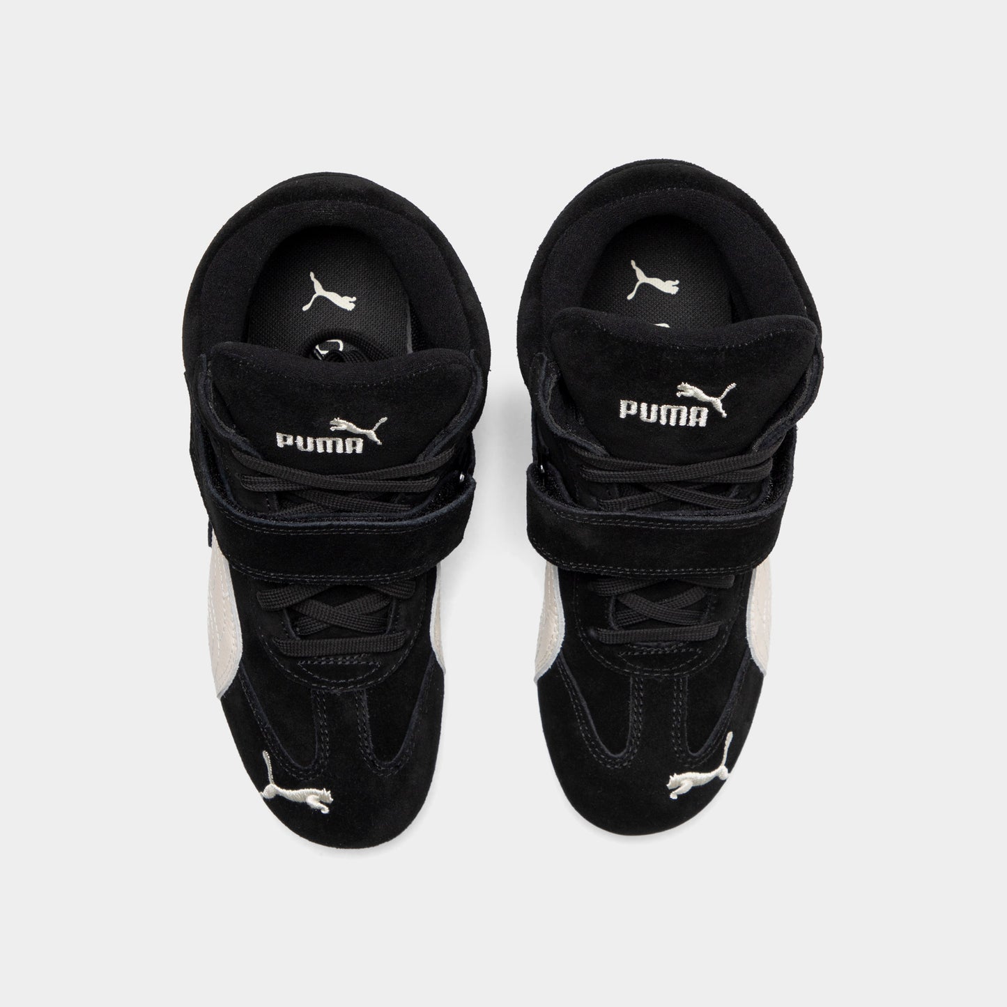 Puma Women's Speedcat Wedge. Top view of black and white wedge sneakers showing padded tongues, hook-and-loop straps and black insoles.
