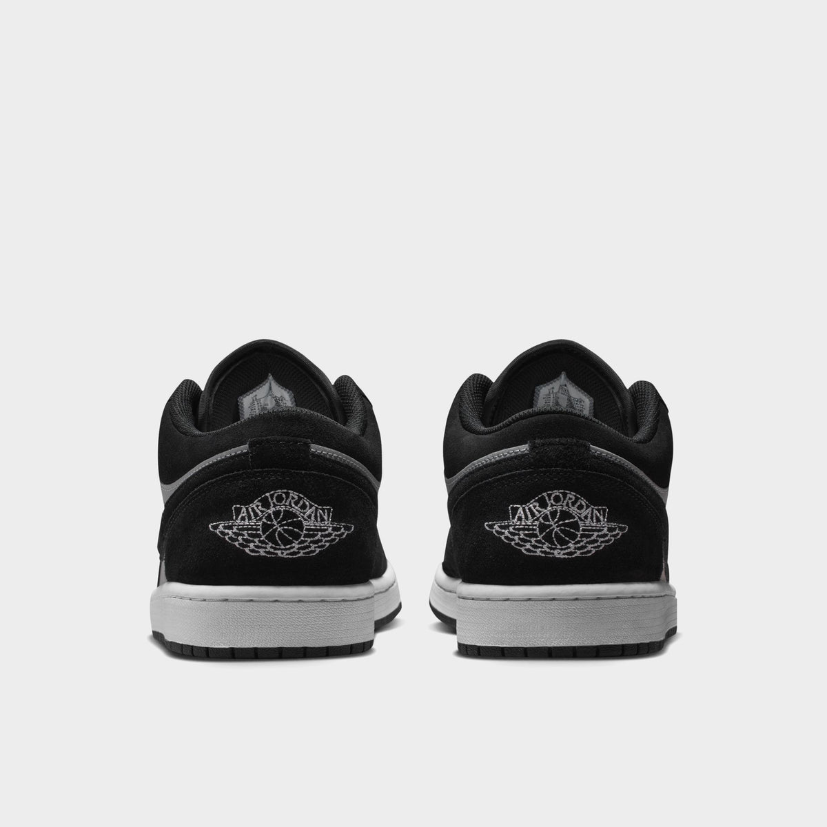 Jordan 1 Low. Rear view of black, white and light smoke grey sneakers with black heel panels, grey branding and white midsoles.