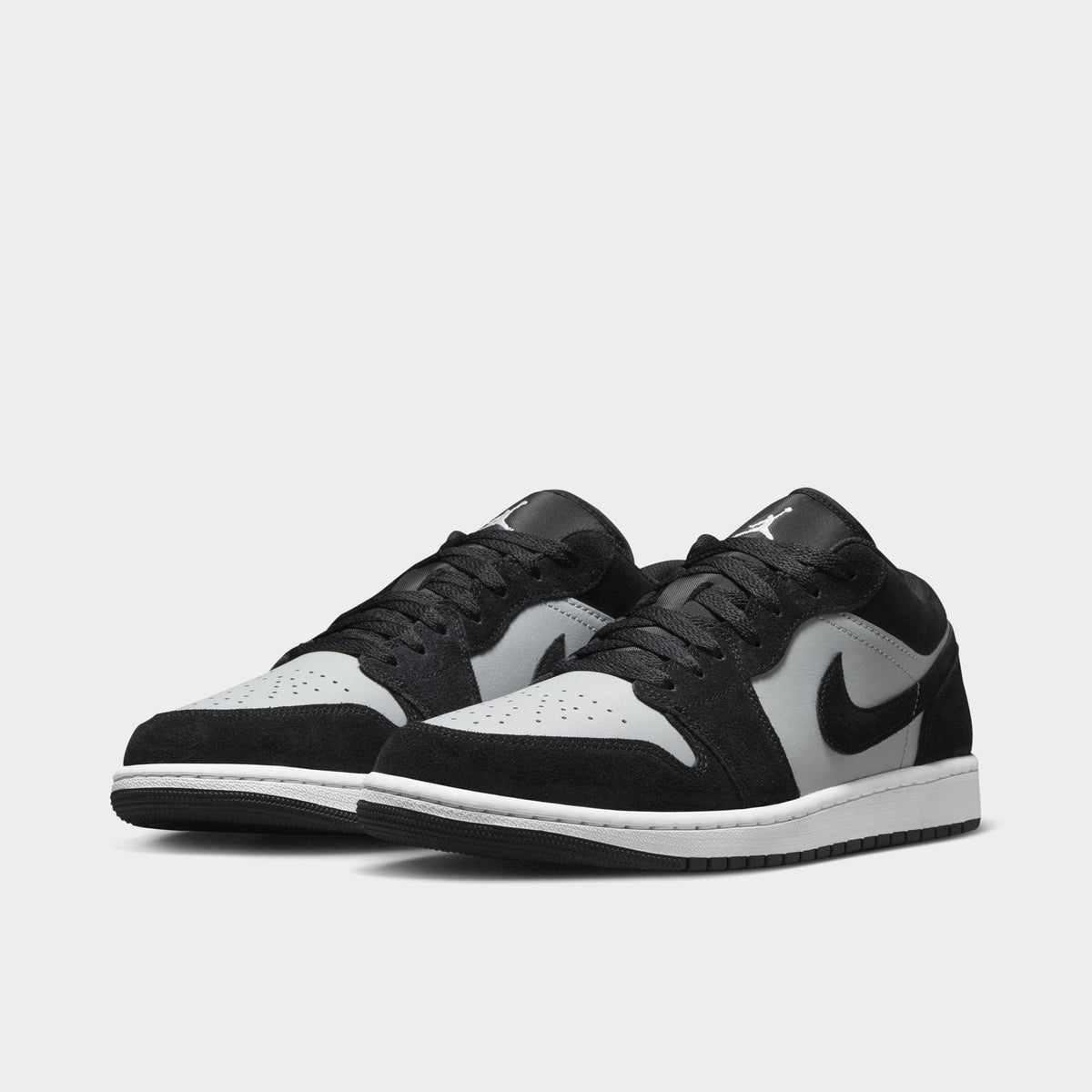 Jordan 1 Low. Three-quarter view of black, white and light smoke grey sneakers with black laces, grey Swooshes and white toe boxes.
