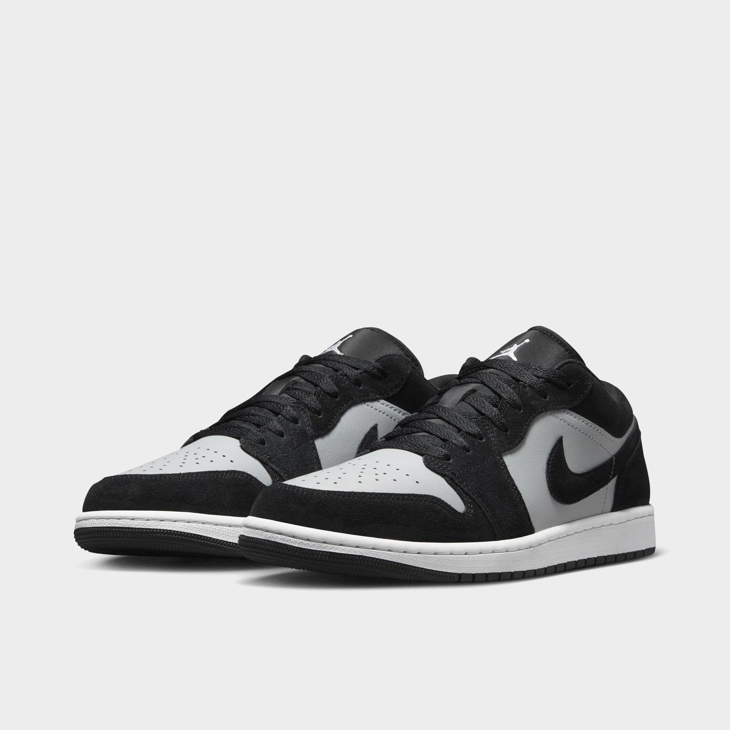 Jordan 1 Low. Three-quarter view of black, white and light smoke grey sneakers with black laces, grey Swooshes and white toe boxes.