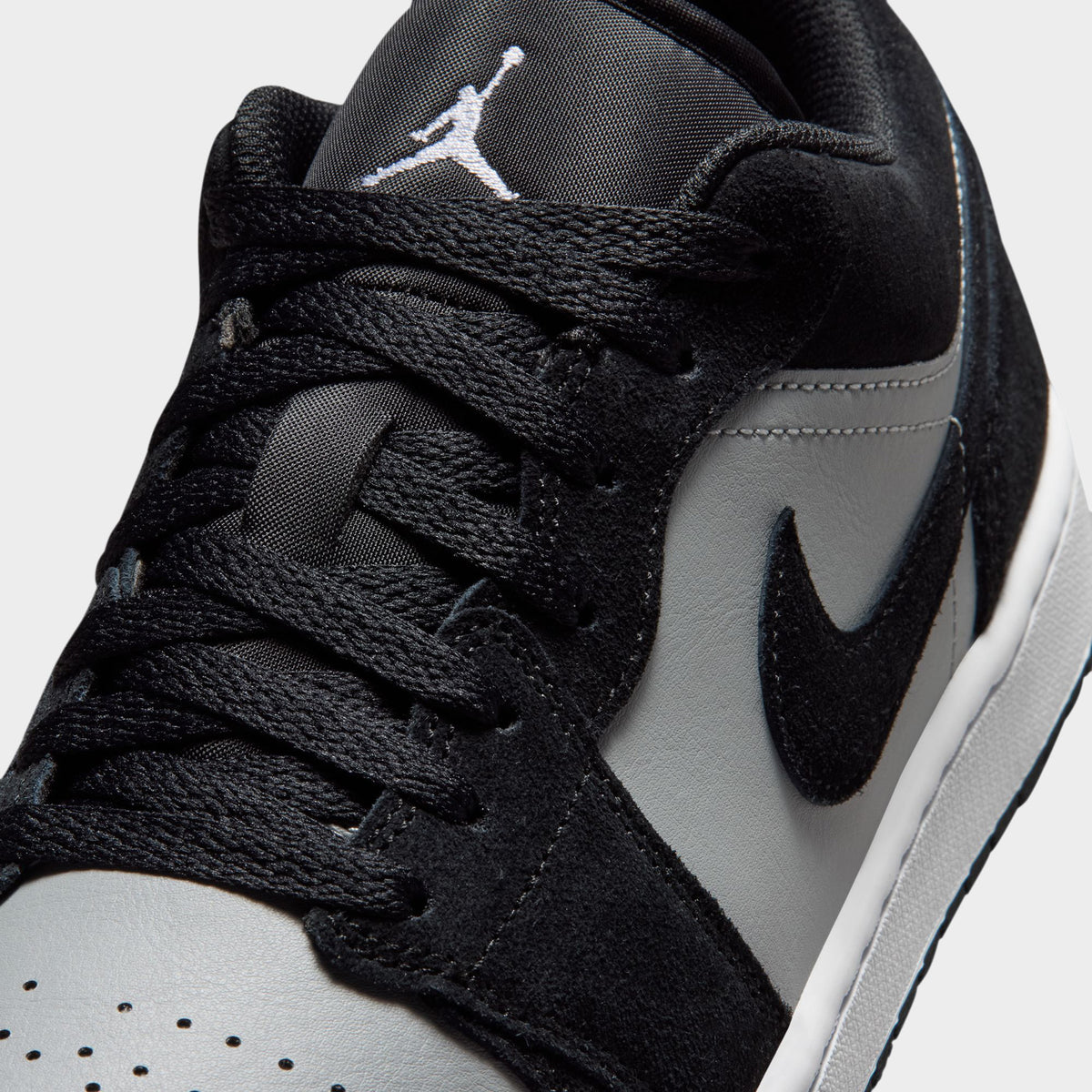 Jordan 1 Low. Close-up of black, white and light smoke grey sneaker showing black laces, perforated white toe box and grey Swoosh.