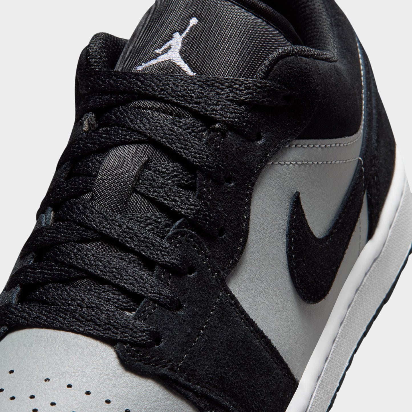 Jordan 1 Low. Close-up of black, white and light smoke grey sneaker showing black laces, perforated white toe box and grey Swoosh.