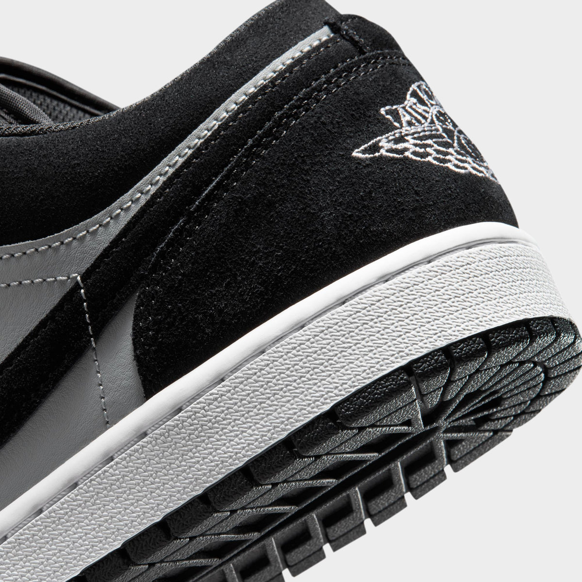 Jordan 1 Low. Close-up of black, white and light smoke grey sneaker showing black heel panel, embroidered branding and textured outsole edge.