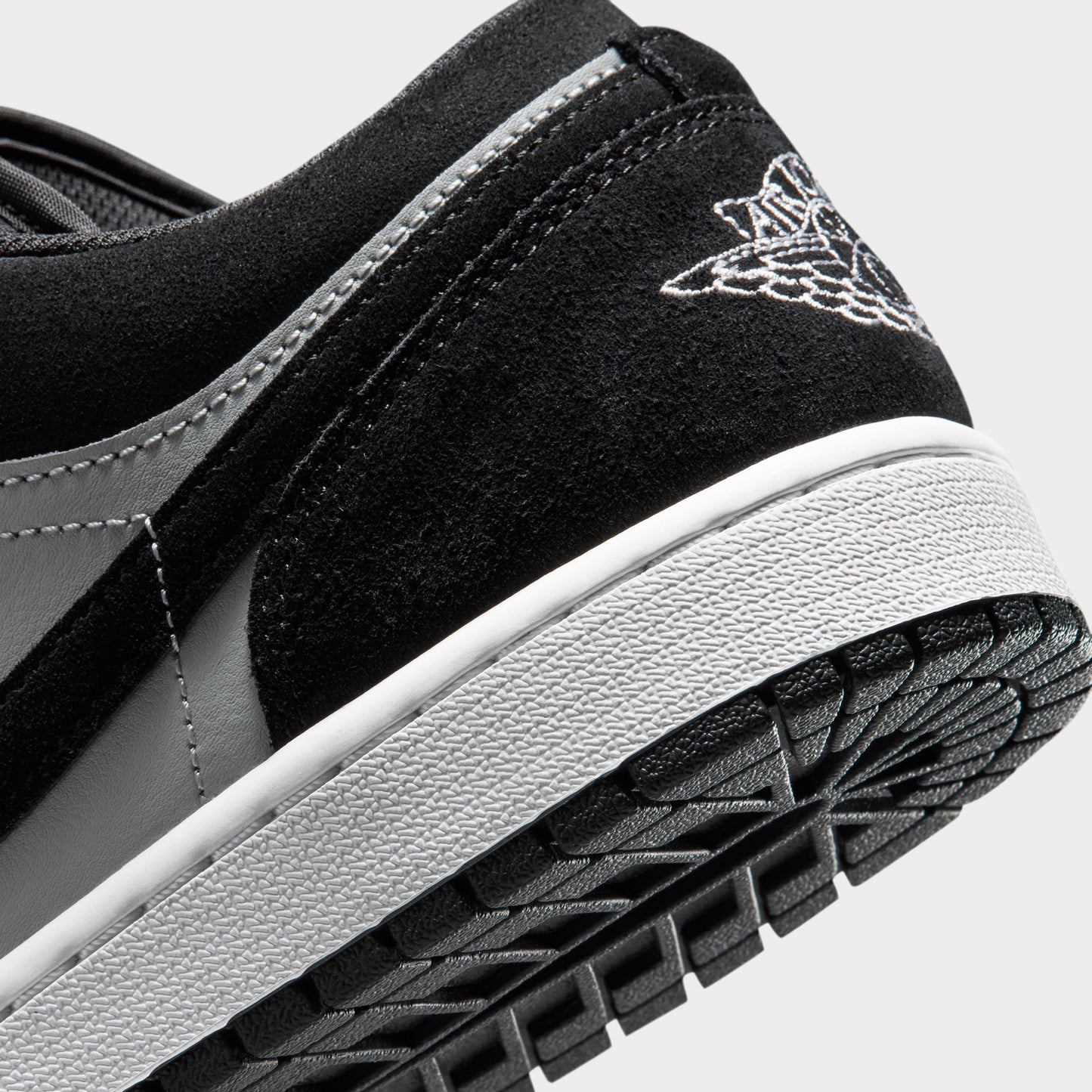 Jordan 1 Low. Close-up of black, white and light smoke grey sneaker showing black heel panel, embroidered branding and textured outsole edge.