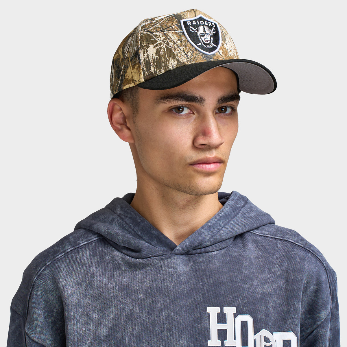 New Era Las Vegas Raiders 9FORTY A-Frame cap. Front view of model wearing a Realtree camo and black cap with a curved black brim and Las Vegas Raiders shield logo patch on the front.