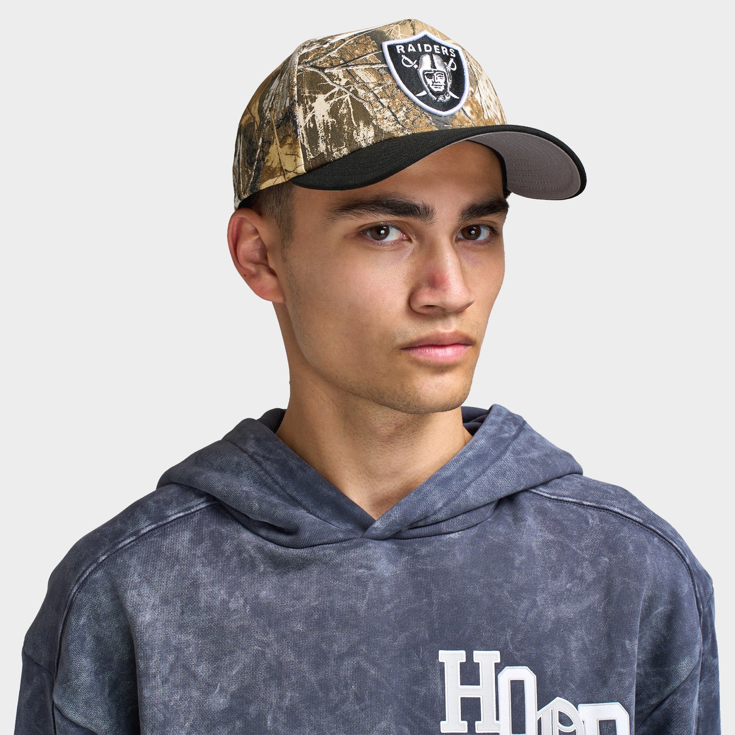 New Era Las Vegas Raiders 9FORTY A-Frame cap. Front view of model wearing a Realtree camo and black cap with a curved black brim and Las Vegas Raiders shield logo patch on the front.