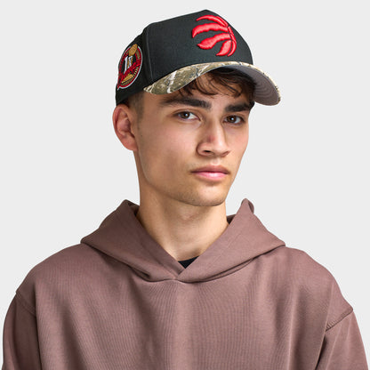 New Era Toronto Raptors 9FORTY AF Snapback. Front view of model wearing black and camo cap with camouflage curved brim, red Raptors logo and side patch.