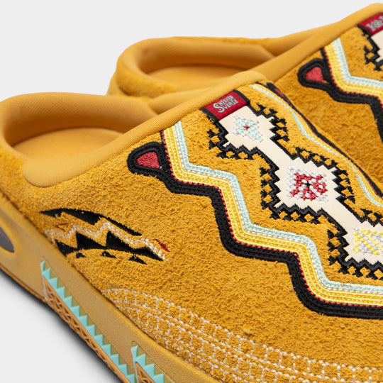 ANTA Kai 2 Slide. Close-up of mustard suede slide showing layered embroidery, red and black accents and turquoise trim.