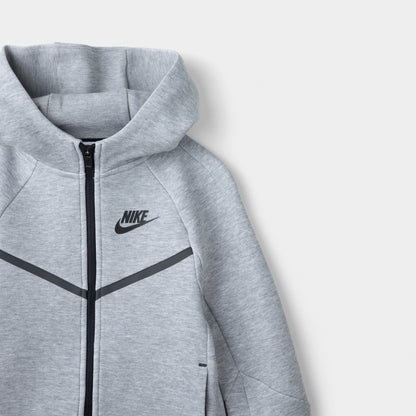 Nike Sportswear Children's Tech Fleece Full Zip Hoodie Set. Close-up of dark grey heather hoodie showing the hood, full-zip closure, black piping and Nike chest logo.