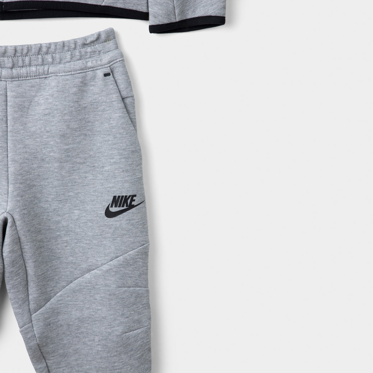 Nike Sportswear Children's Tech Fleece Full Zip Hoodie Set. Close-up of dark grey heather joggers showing the elastic waistband, black Nike logo and tapered leg.